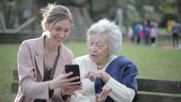 A younger person shows an older person something on the phone