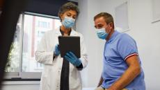 Doctor in mask showing tablet to patient in mask
