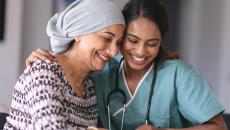 A clinician and a cancer patient with a head scarf smile as they look down.