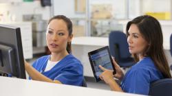 Healthcare worker with tablet looking at screen another worker is pointing at