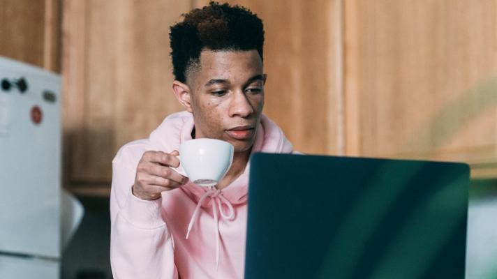 A person using a computer and holding a teacup