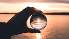 Hand holds a crystal ball before a sunset scene that is reflected inside the ball.